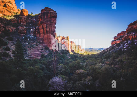 Atemberaubende Aussicht auf Fay Canyon von oben die Baumkronen mit Patches von Schnee auf dem Boden und majestätischen Blick auf Bell Rock und den Courthouse Butte in der Dis Stockfoto