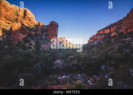 Atemberaubende Aussicht auf Fay Canyon von oben die Baumkronen mit Patches von Schnee auf dem Boden und majestätischen Blick auf Bell Rock und den Courthouse Butte in der Dis Stockfoto