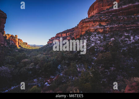 Atemberaubende Aussicht auf Fay Canyon von oben die Baumkronen mit Patches von Schnee auf dem Boden und majestätischen Blick auf Bell Rock und den Courthouse Butte in der Dis Stockfoto