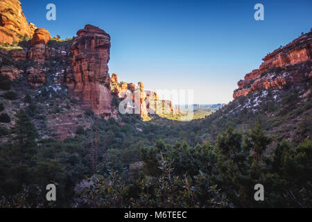 Atemberaubende Aussicht auf Fay Canyon von oben die Baumkronen mit Patches von Schnee auf dem Boden und majestätischen Blick auf Bell Rock und den Courthouse Butte in der Dis Stockfoto