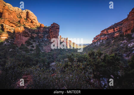 Atemberaubende Aussicht auf Fay Canyon von oben die Baumkronen mit Patches von Schnee auf dem Boden und majestätischen Blick auf Bell Rock und den Courthouse Butte in der Dis Stockfoto