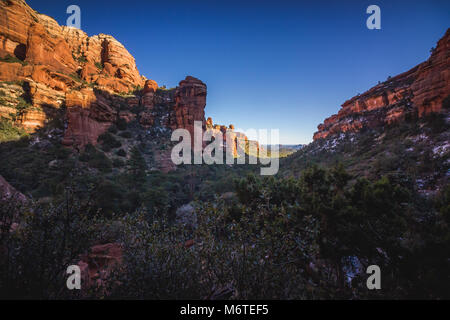 Atemberaubende Aussicht auf Fay Canyon von oben die Baumkronen mit Patches von Schnee auf dem Boden und majestätischen Blick auf Bell Rock und den Courthouse Butte in der Dis Stockfoto