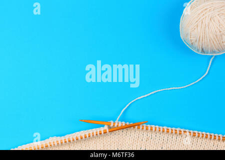 Knitting with wooden knitting needles and wool yarn ball on blue background Stockfoto