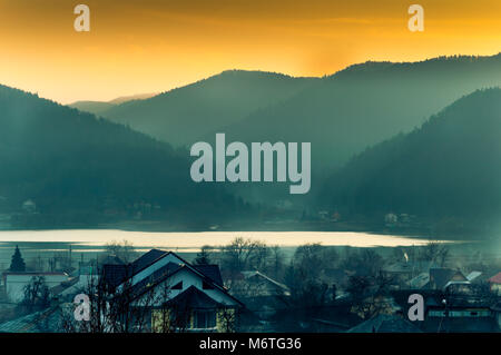 Berge Sonnenuntergang und Nebel Landschaft. Nebelig mystische Abend über das Dorf. Stockfoto