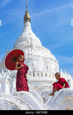 Junge Novizin buddhistische Mönche, einer Holding- und einem Sonnenschirm sitzen an Myatheindan Pagode (auch als Hsinbyume Pagode bekannt), Mingun, Myanmar (Birma) Asien Stockfoto