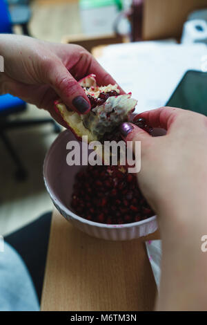 Frau im Büro peeling öffnen Sie einen Granatapfel mit ihren Händen über eine weiße Schüssel Stockfoto