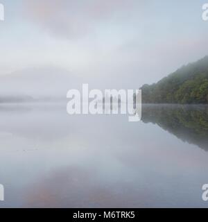 Ein sehr nebligen herbstlichen Morgen auf Loch Achray. Ich nahm diese so wie die Sonne die Wolken rosa aber der Nebel verbreitet die Szene sehr gut. Stockfoto