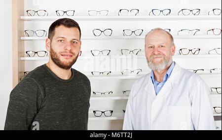 Reifen Augenarzt mit jungen Mann die Wahl Eyeglass frame in optischen Speichern Stockfoto