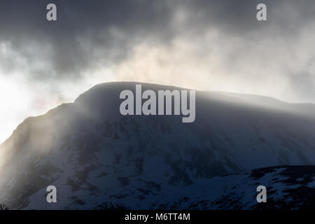 Vom Westen aus gesehen, die Sonne bricht durch stürmische Wolken Schnee auf dem Gipfel des Ben Nevis (in den Highlands von Schottland), der höchste Berg in der U Stockfoto