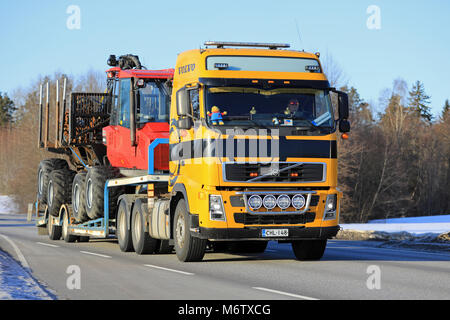 SALO, Finnland - 2. MÄRZ 2018: Gelb Volvo FH semi Transporte Wald Traktor auf Anhänger auf der Autobahn an einem sonnigen Tag der Winter im Süden Finnlands. Stockfoto