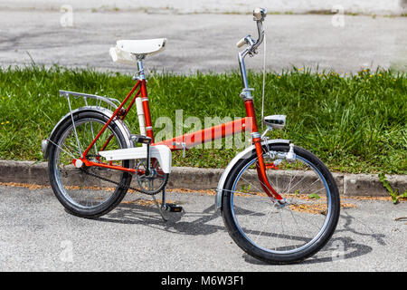 Vintage Classic 1970 s rotes Klapprad Fahrrad in einem einwandfreien Zustand Parken auf der Straße in der Nähe von Gras Stockfoto