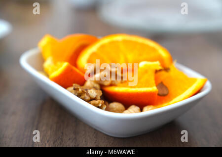Orange in Scheiben und Muttern zusammen in eine Schüssel geben. Stockfoto