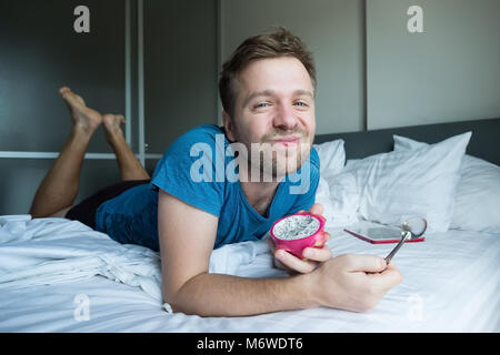 Kaukasische Mann essen Dragon fruie mit Löffel im Bett. Stockfoto
