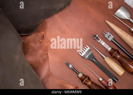 Tools für Leder basteln und Stücke von braunem Leder. Herstellung von Lederwaren. Ansicht von oben Stockfoto