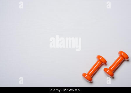 Zwei kurzhanteln von Orange liegen auf einem weißen Hintergrund mit einem Baum Textur. Stockfoto