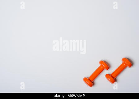Zwei kurzhanteln von Orange liegen auf einem weißen Hintergrund mit einem Baum Textur. Stockfoto