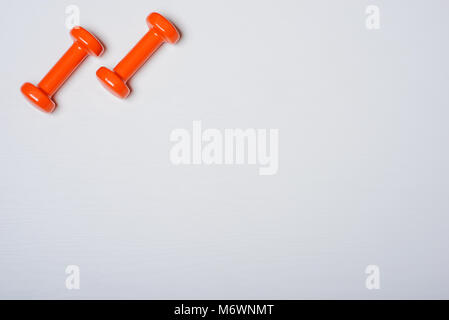 Zwei kurzhanteln von Orange liegen auf einem weißen Hintergrund mit einem Baum Textur. Stockfoto
