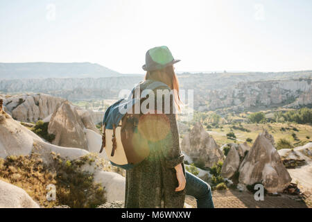 Ein Reisender in einen Hut mit einem Rucksack steht auf einem Berg und blickt auf einen wunderschönen Blick in Kappadokien in der Türkei. Reise. Wandern. Stockfoto