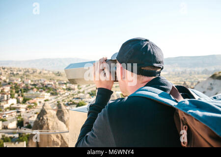 Ein Reisender mit einem Rucksack auf Sicht sieht durch ein Fernglas bei einem schönen Blick auf die Stadt von Göreme in Kappadokien in der Türkei. Reise. Wandern. Stockfoto