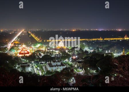 Panoramablick über die beleuchtete Kyauktawgyi Pagode, andere Gebäude, Wassergraben Mandalay Palace und darüber hinaus von der Mandalay Hill in Mandalay, Myanmar in der Nacht. Stockfoto