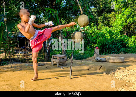 Ein sieben Jahre alter Junge Schulung seiner kickboxing Skills wird durch Kicken Bälle Stockfoto