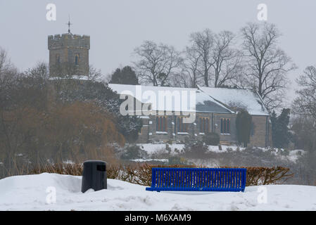 Ein helles Blau öffentliche Bank unbrauchbar wegen starker Schneefall in den Vordergrund der Blick auf die Kirche des Hl. Laurentius, Henley upon-Avon, Warwickshire. Stockfoto