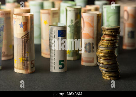 Stapel von Euro-münzen und Rollen von Banknoten im Hintergrund Stockfoto