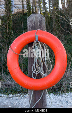 Eine orange Perry Boje oder Leben Boje Gummiring oder floatation Gerät für lebensrettende in der Nähe von Wasser auf einer hölzernen Pfosten mit einem Seil für das Werfen von Wasser. Stockfoto