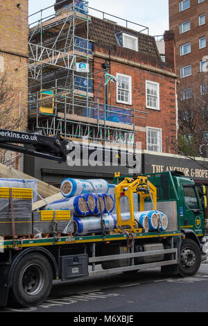 Eine Konstruktion oder Erbauer Händler Lieferung Lkw auf einer Baustelle am Straßenrand liefert Materialien zu einer Site mit Gerüst bauen geparkt. Stockfoto