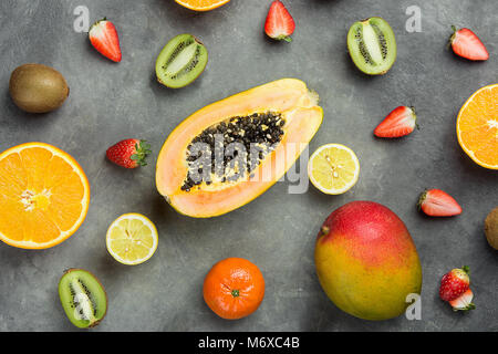 Verschiedene Tropische und saisonale Sommer Früchte. Papaya Mango Tangerinen Zitronen Orangen Zitronen Erdbeeren, Kiwi verstreut auf dunklem Hintergrund Stockfoto