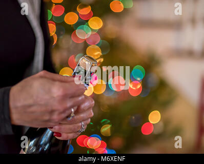 Nahaufnahme einer Frau das Öffnen einer Flasche Champagner Rosé auf Silvester mit Bokeh christmas lights im Hintergrund Stockfoto
