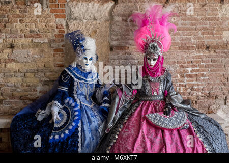 Zwei Frauen in Masken und kunstvollen blau und rosa Kostüme und dekorative Ventilatoren, sitzt auf einer Steinbank gegen eine alte Mauer. Stockfoto