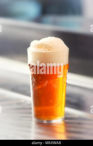 Frisch serviert Pint schaumiges Bier mit einem guten Kopf in einem Glas auf einer Metallstange Zähler in einer Nahaufnahme, Seitenansicht Stockfoto
