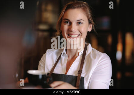 Lächelnde Frau Kaffee in einem Café. Happy coffee shop besitzer Halten einer Tasse Kaffee im Shop. Stockfoto