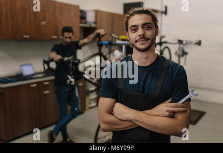 Arbeitnehmer stehen mit verschränkten Armen Holding einen Schraubenschlüssel in der Werkstatt. Mechanik fahrräder Zusammenbau in der Werkstatt. Stockfoto