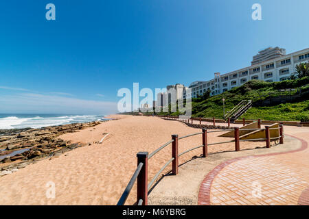 Gepflasterte Strandpromenade Strand Sand Felsen und Meer Wellen gegen blaue Küste Skyline der Stadt in Umhlanga, Durban, Südafrika Stockfoto