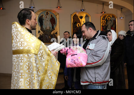 Taufe für Baby in der ländlichen Kirche. Priester, der vor Frau und Mann mit einem Baby auf den Händen steht und die Bibel liest. Januar 7,2018. Bucha, Ukraine Stockfoto