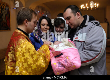 Taufe für Baby in einer ländlichen Gemeinde. Mann und Frau mit einem Baby auf Hände und ein Priester standingnear. 7. Januar 2018. Bucha Dorf, Ukraine Stockfoto