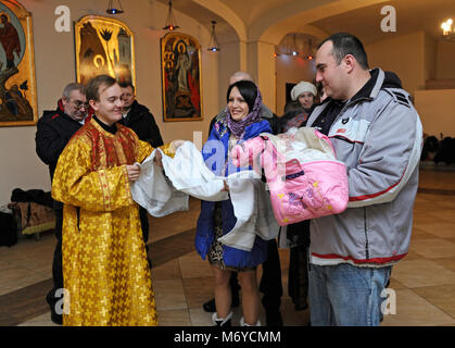 Taufe für Baby in einer ländlichen Gemeinde. Mann und Frau mit einem Baby auf Hände und ein Priester standingnear. 7. Januar 2018. Bucha Dorf, Ukraine Stockfoto