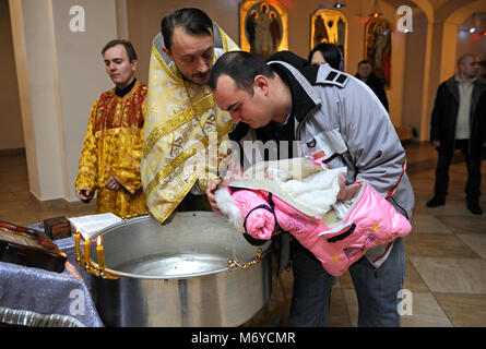 Taufe für Baby in einer ländlichen Kirche. Priester, der vor einem Mann mit einem Baby auf den Händen steht und ein Kind tauft. 7. Januar 2018. Bucha, Ukraine Stockfoto