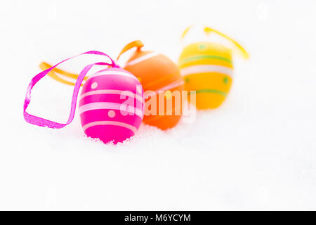 Nahaufnahme von rosa, orange und Gelb Ostern Eier mit Bändern und mit Streifen und Punkte Festlegung im Freien auf frischen Schnee im Frühjahr eingerichtet Stockfoto