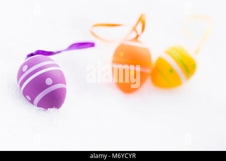 Nahaufnahme von lila, orange und gelbe Ostereier mit Bändern und mit Streifen und Punkte Festlegung im Freien auf frischen Schnee im Frühjahr eingerichtet Stockfoto