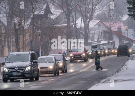 Karpacz, Polen - Februar 2018: die Menschen überqueren die Straße auf einem Zebrastreifen Inmitten starker Verkehr auf der Straße in der polnischen Skigebiet nach schweren snowf Stockfoto