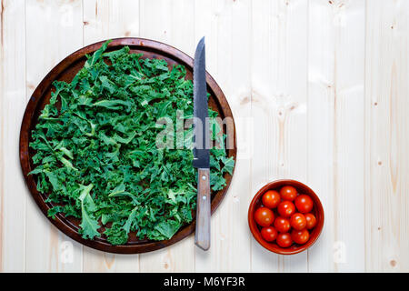 Frisch gehackten Grünkohl vorbereitet auf alte Metall Platte mit Messer mit Schüssel Kirschtomaten für Salat oder Smoothie mit Kopie Raum Stockfoto