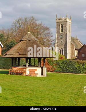 Ein Blick auf die Kirche St. Fabian und St. Sebastian und Reet gedeckten Brunnen auf dem Dorfplatz an Woodbastwick, Norfolk, England, UK. Stockfoto