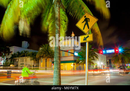 Straßen von Miami bei Nacht mit Palmen und Ampel. Radfahrer an der Kreuzung warten. Stockfoto