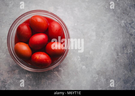 Satz von sechs Farben Rot, in eine Glasschale für Ostern, Färbung mit Rotstich Eier über einen konkreten Hintergrund, grau Stockfoto