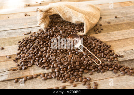 Geröstete Kaffeebohnen in einem sackleinen Beutel auf hölzernen Tisch Hintergrund mit Kupfer Lufthutze Stockfoto