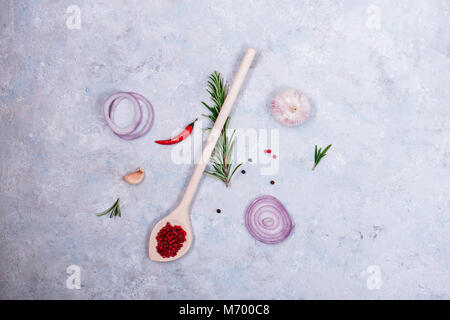 Gewürze auf dem Tisch - Rosmarin, rote Zwiebel, Knoblauch und Paprika in einem Löffel aus Holz Stockfoto