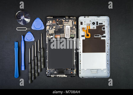 Arbeitsplatz der Handwerker mit den Telefon- und Sonderwerkzeuge auf dem Schwarzen Tisch. Zerlegt Smartphone in flatlay Stil. Stockfoto